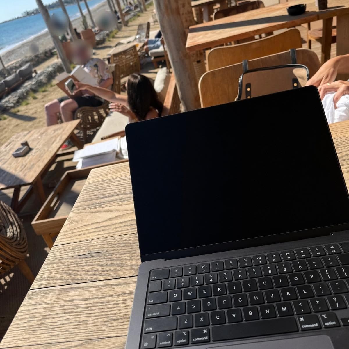 A laptop on a wooden table at a beach bar, with the sea in the background
