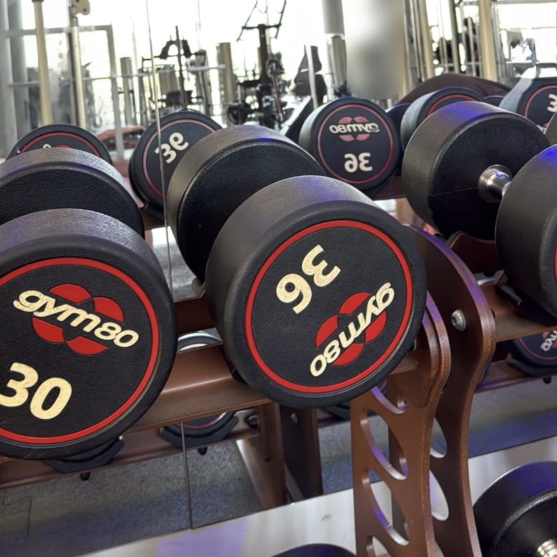 Rows of black dumbbells on a rack in a gym, with the training floor reflected in a mirror